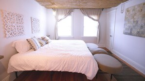 A bedroom with a bed, two windows with curtains, a wall with decorative panels, and a textured ceiling. - Rustic cottage-style condo within walking distance to downtown Homewood (Homewood)