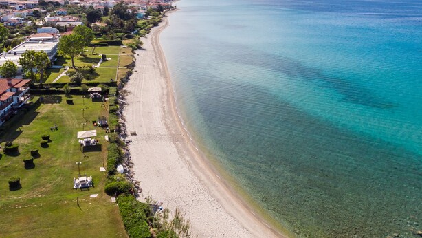 Ett flygbildsbild av ett kustområde med en strand, bostadshus och klart, blått vatten.