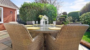 A patio with a round table and wicker chairs, surrounded by greenery and a brick building. - Wix, with its rolling countryside and reputation as a peaceful village, perfect for a rural stay (Manningtree)