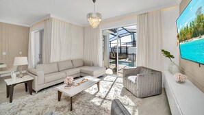 Ein modernes Wohnzimmer mit einem beigefarbenen Sofa, einem Couchtisch und einem Fernseher auf einer weißen Konsole.