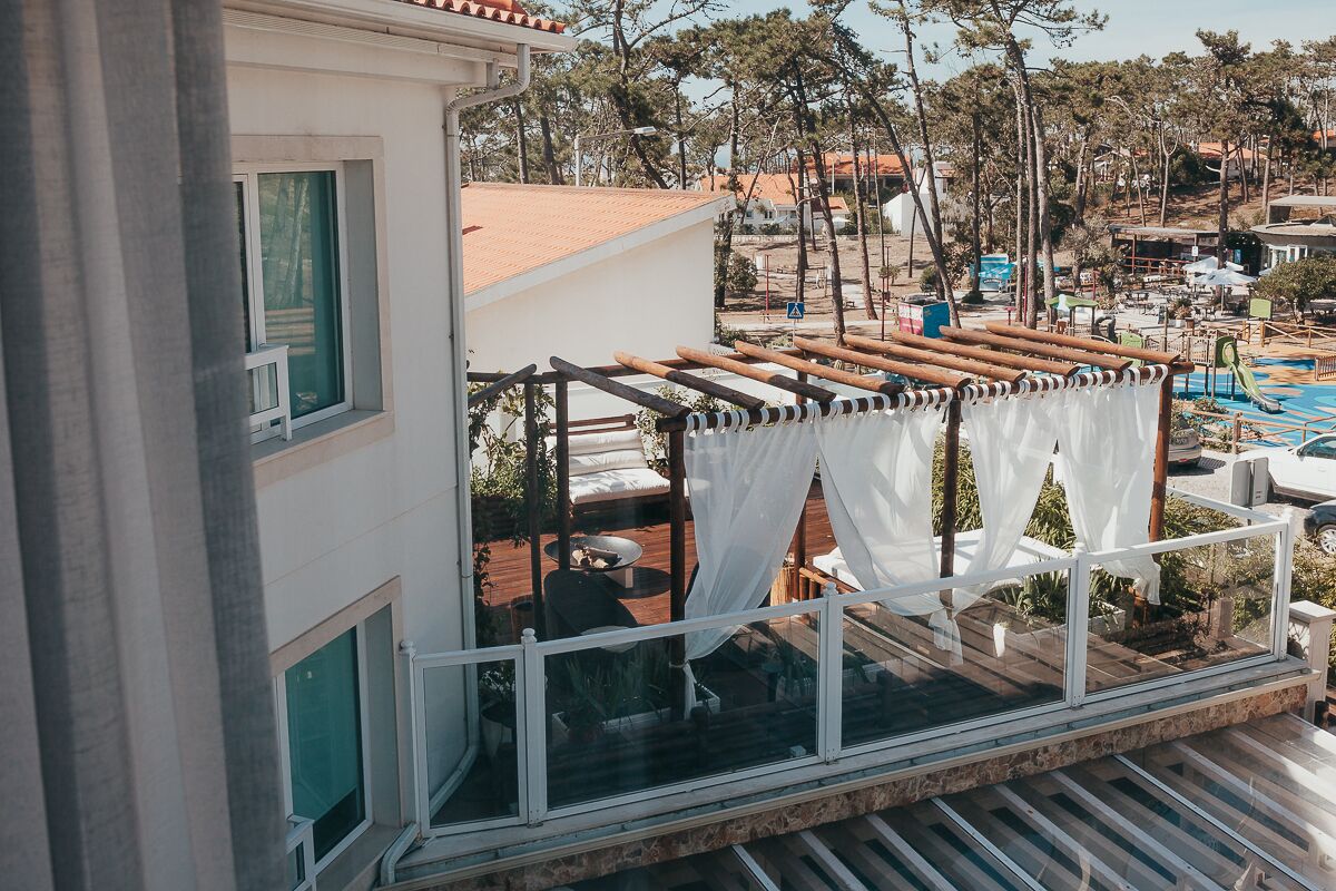 A balcony with a pergola, a pool, and a view of a resort area.