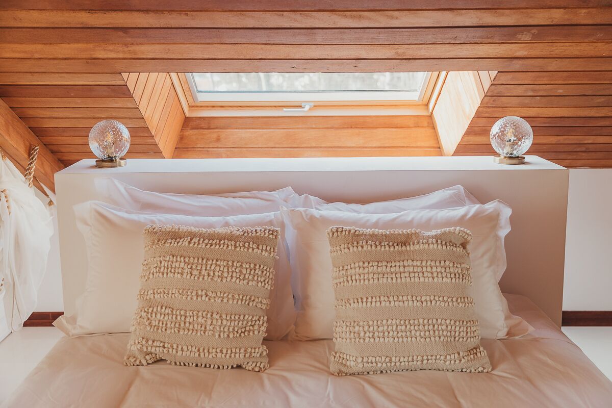 Une chambre avec un plafond en pente, des poutres en bois, deux objets décoratifs sphériques posés sur la tête de lit et deux coussins à texture.