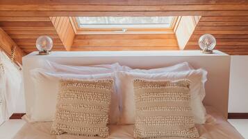 Une chambre avec un plafond en pente, des poutres en bois, deux objets décoratifs sphériques posés sur la tête de lit et deux coussins à texture.