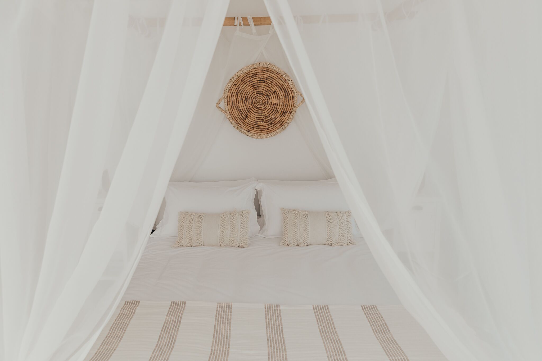 Ein Bett mit weißer Bettwäsche und einem Kopfbrett aus Gewebe, umgeben von transparenten weißen Vorhängen.
