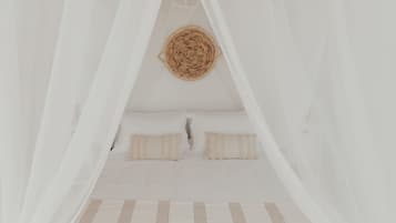 Ein Bett mit weißer Bettwäsche und einem Kopfbrett aus Gewebe, umgeben von transparenten weißen Vorhängen.