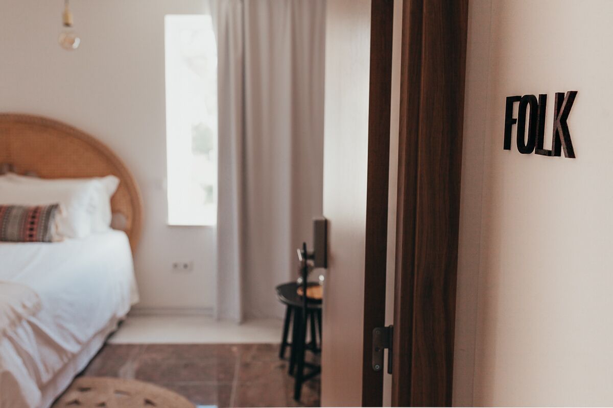 A bedroom with a bed, a small table, and a chair. There is a door with the word "FOLK" on it.