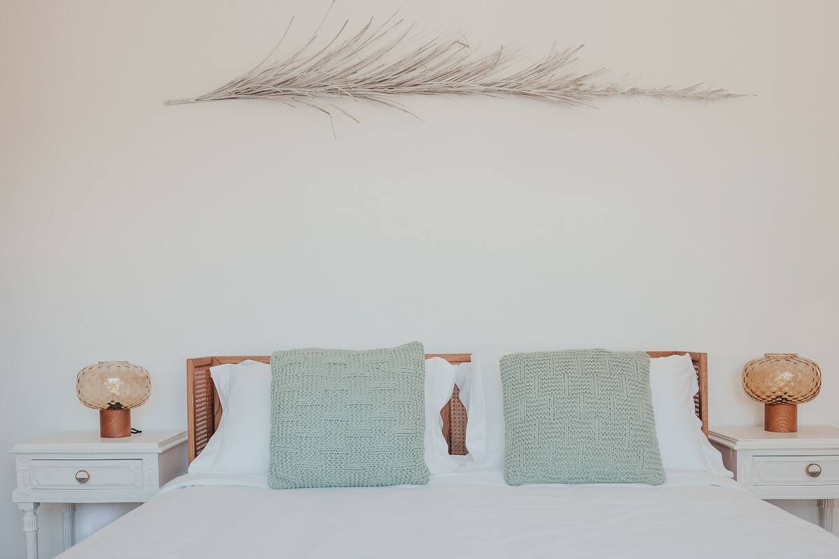 Una cama bien hecha con dos almohadas y una rama decorativa encima.