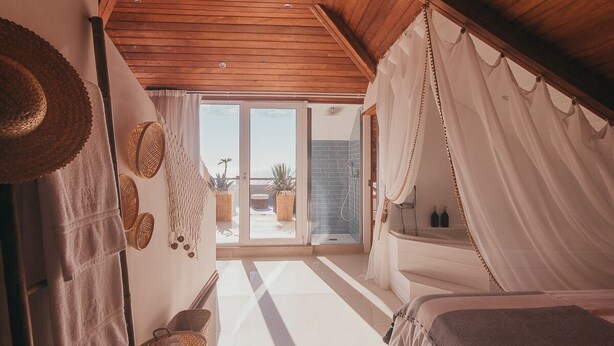 Ein Schlafzimmer mit Bett, großem Fenster und Blick ins Freie.
