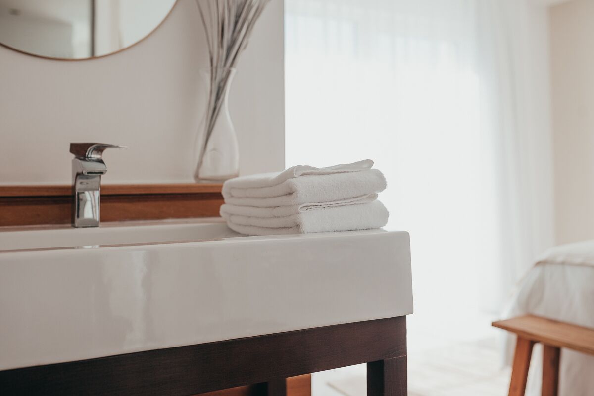 A bathroom with a white sink, a mirror, and a stack of white towels.