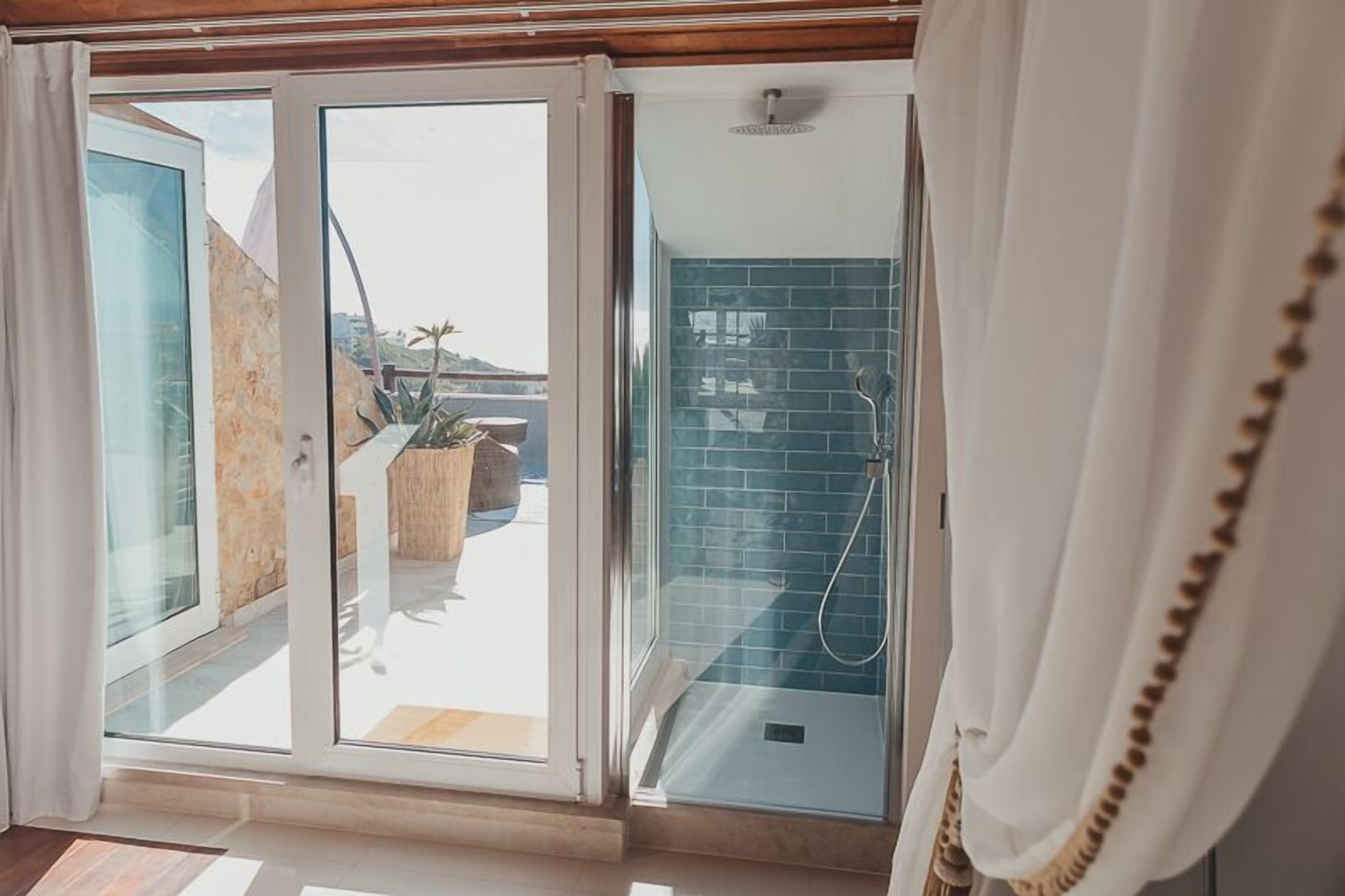 Une salle de bain moderne avec une porte en verre donnant sur un balcon, un espace douche avec des carreaux bleus et un plancher en bois.