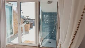 Une salle de bain moderne avec une porte en verre donnant sur un balcon, un espace douche avec des carreaux bleus et un plancher en bois.