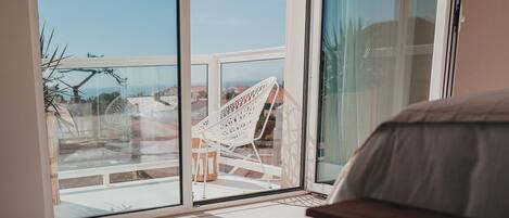 A balcony with a white chair, a small table, and a view of the cityscape.