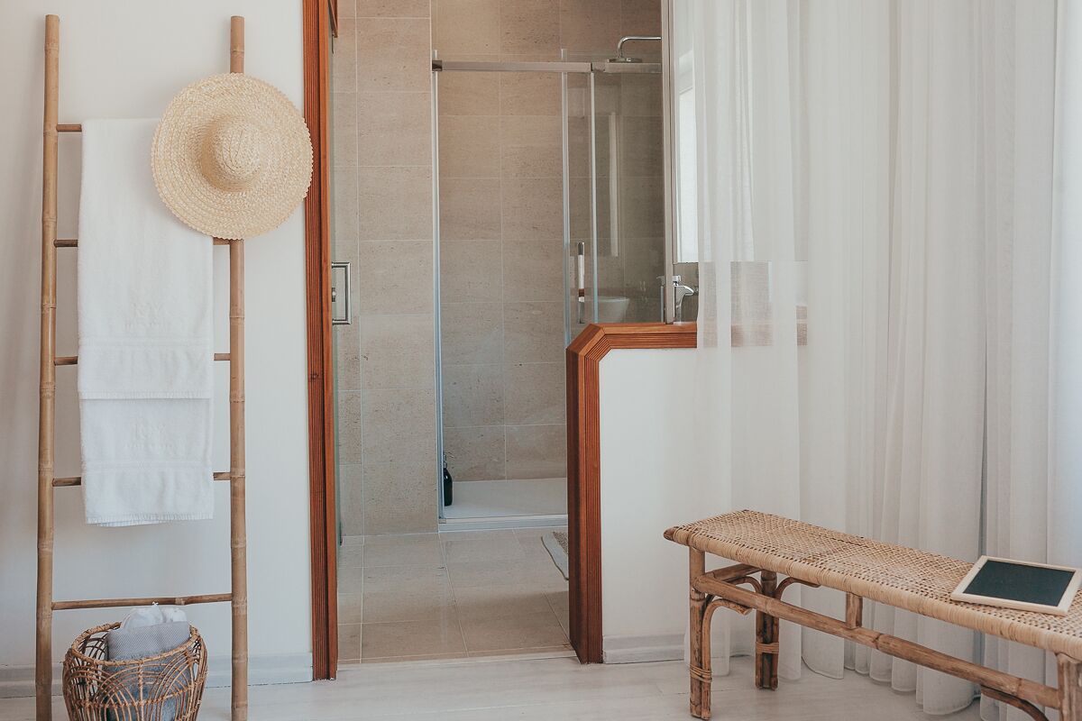 Casa de banho com uma escada de bambu, um chapéu de palha, uma cadeira de vime e zona de duche.