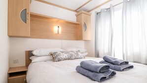 Quarto de hotel com uma cama, mesa de cabeceira, guarda-roupa de madeira e janela com cortinas.