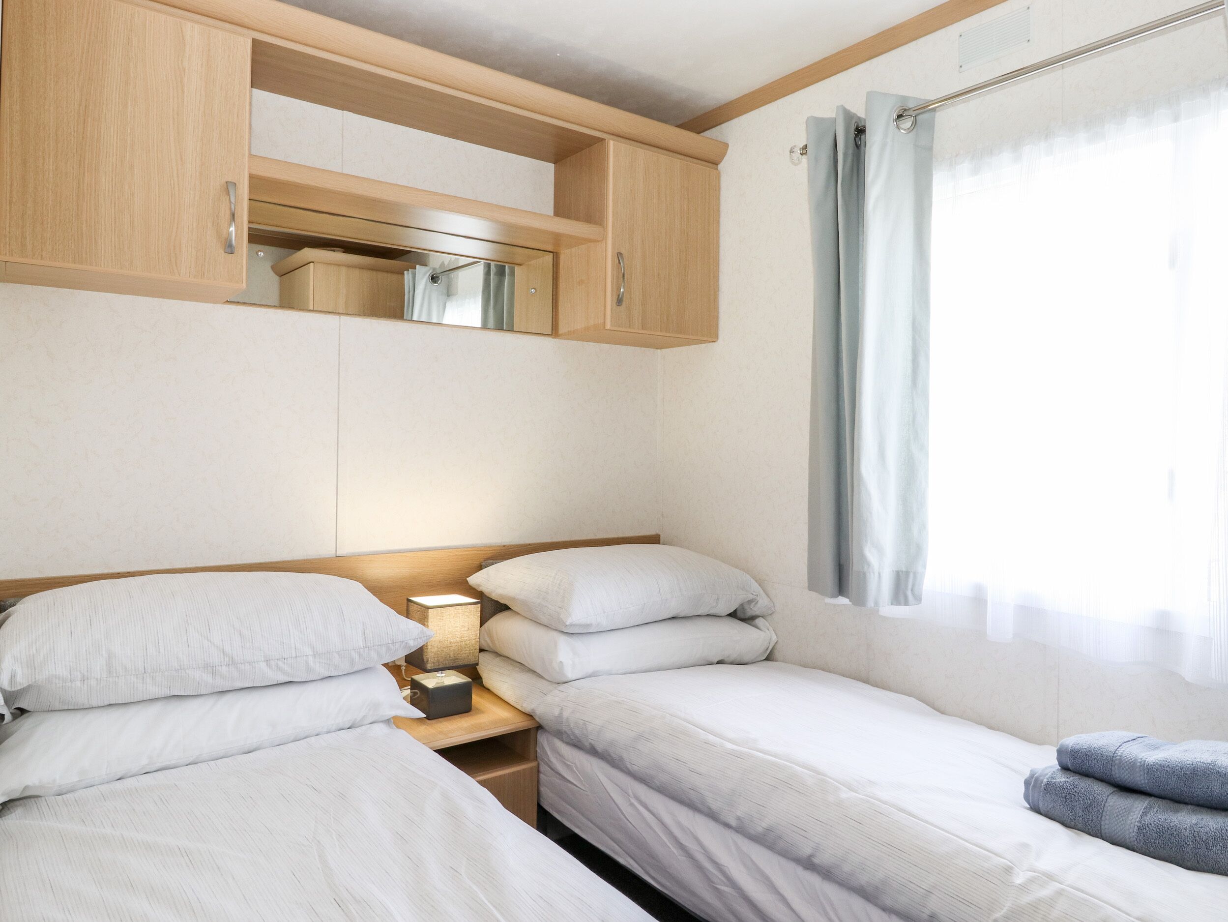 Ein Schlafzimmer mit zwei Einzelbetten, Holzschränken, einem Nachttisch mit Lampe und einem Fenster mit Vorhängen.