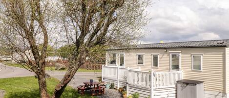 A mobile home with a front deck, a picnic table, and a shed.