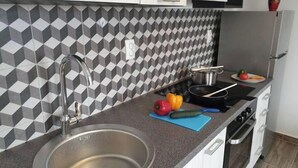 A kitchen with a modern design, featuring a geometric patterned backsplash, a stainless steel sink, a stove, and a countertop with a cutting board and vegetables. - BEST VIEW APARTMENTS CESARICA - DODO (Cesarica)