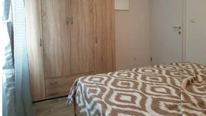 A bedroom with a wooden wardrobe, a bed with patterned bedding, and a white door. - BEST VIEW APARTMENTS CESARICA - DODO (Cesarica)