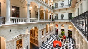 Un atrium à plusieurs niveaux, doté de colonnes blanches, d’un sol à carreaux et de balcons ornés de rampes en fer forgé.