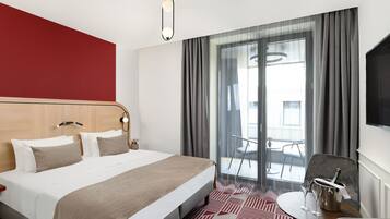 A hotel room with a large bed, a small table with two glasses, a bottle of champagne, and a chair.