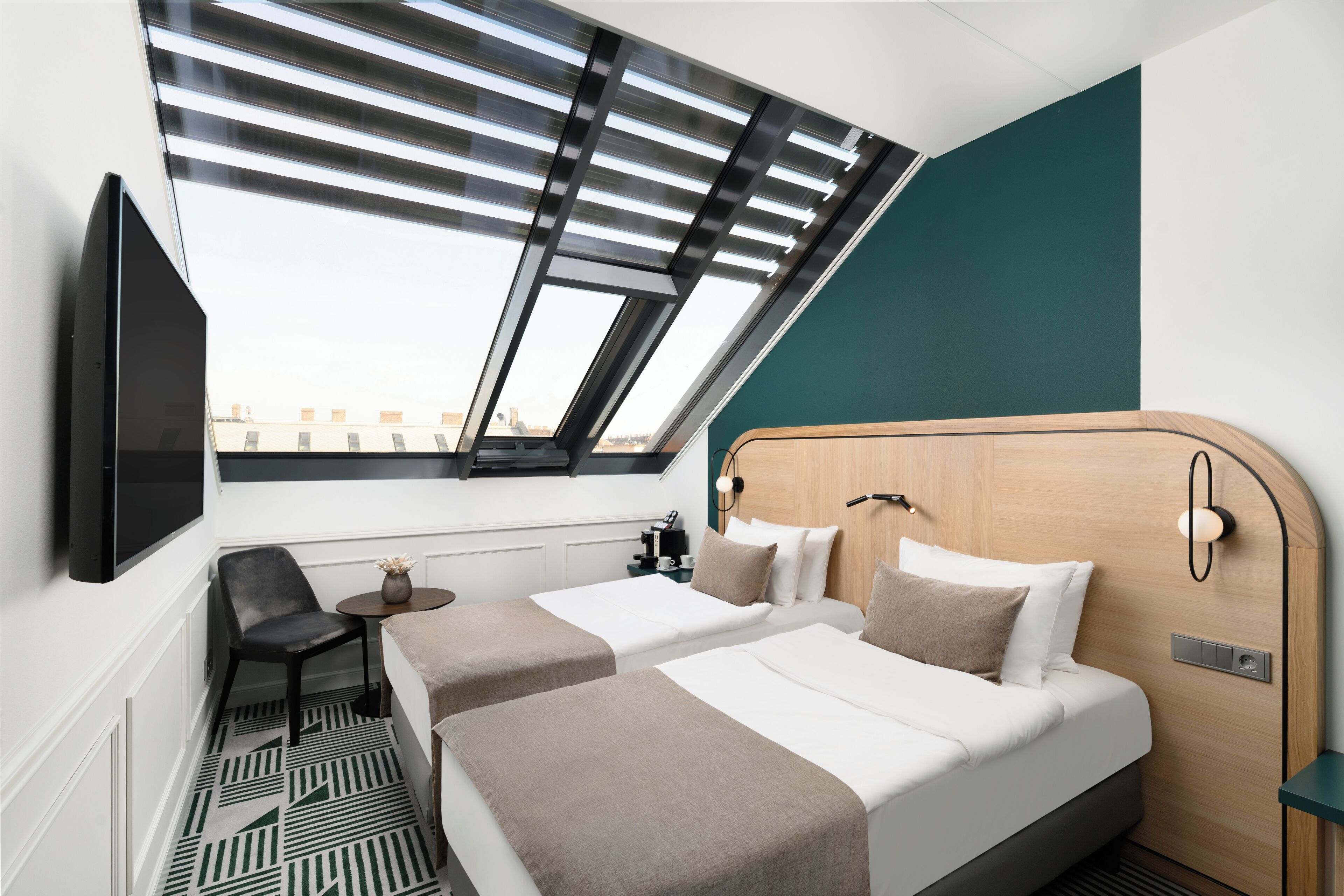 A hotel room with two beds, a TV, a desk, and a window with blinds.