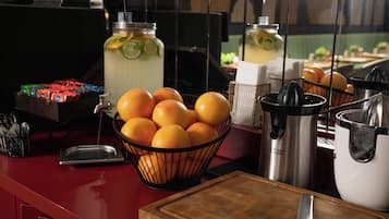 A kitchen counter with a basket of oranges, a juicer, a stainless steel pot, and a jar of lemonade.