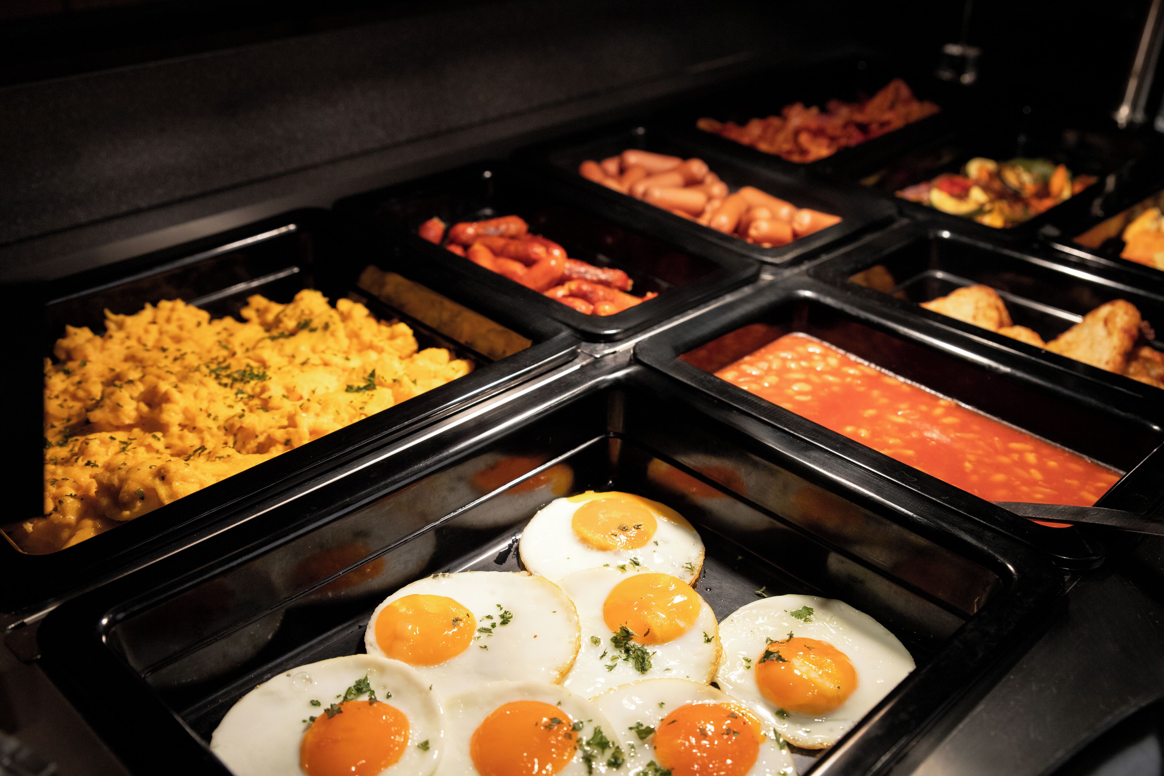 Un bufé con diversas opciones de comida, como huevos, salchichas y otros platos.