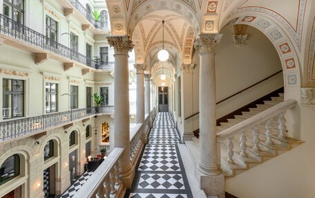 A grand interior with a central hallway flanked by balconies and columns, leading to a staircase.