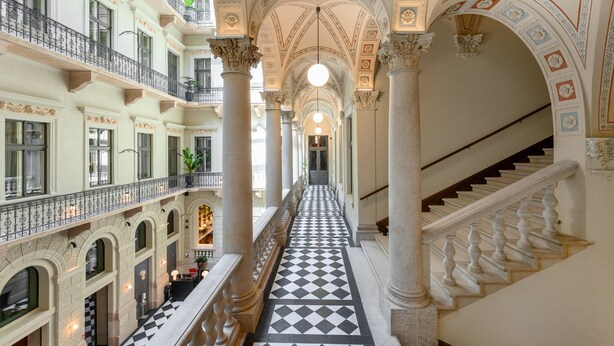 Un vaste espace intérieur avec un couloir central bordé de balcons et de colonnes, qui mène à un escalier.