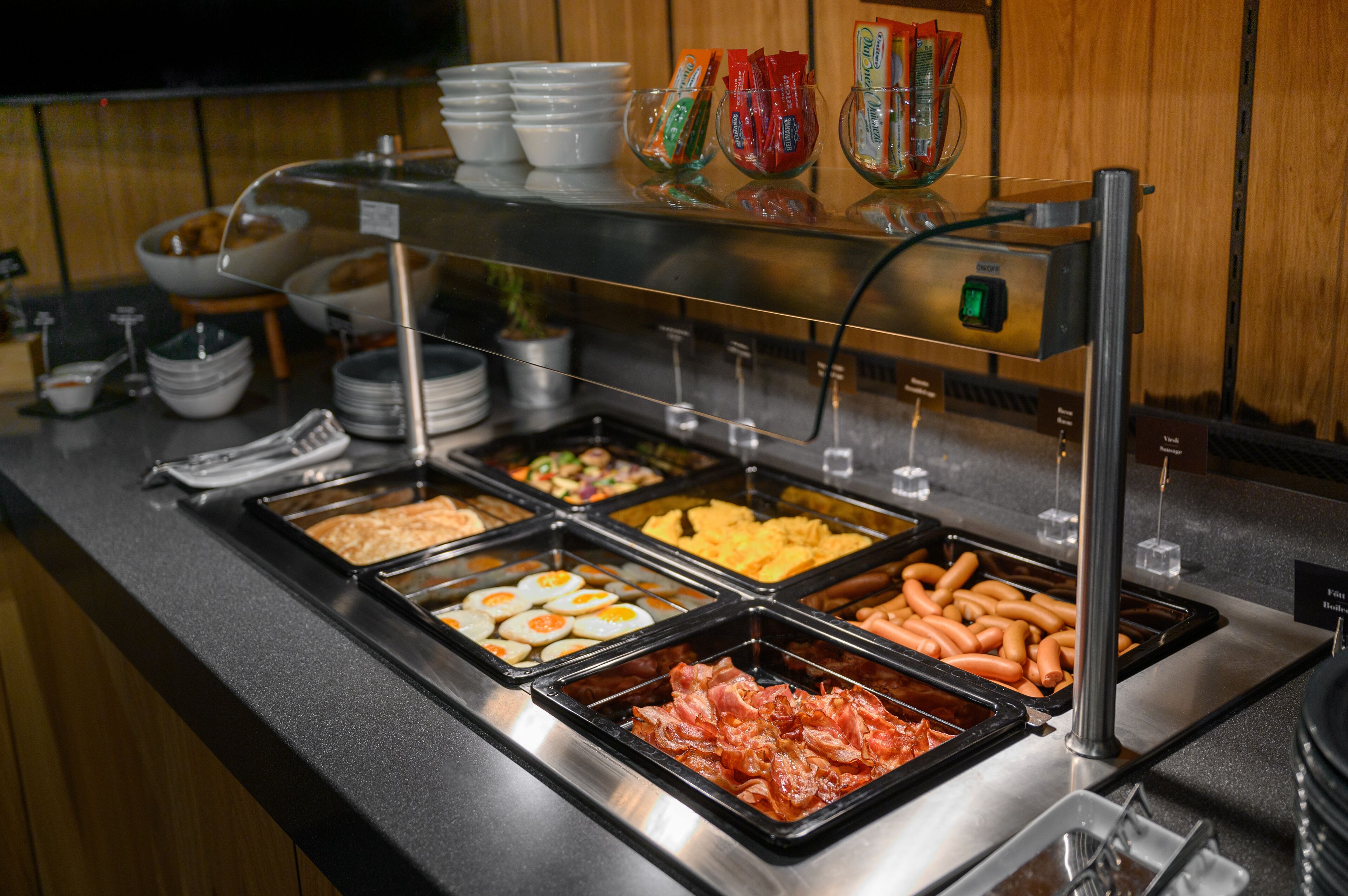 A buffet with various food items including eggs, ham, and hot dogs.