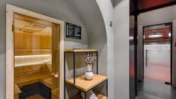 A sauna with a wooden bench and a glass door, a wooden shelf with a vase, and a sign indicating fitness services.