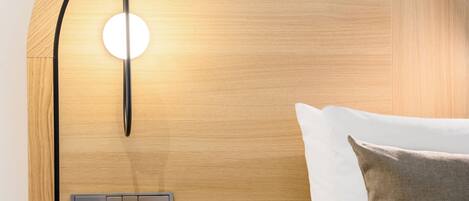Una habitación de hotel moderna con cabecera de madera, una mesita de noche con un florero y una pared de acento roja.