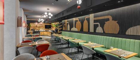 A modern restaurant interior with green booths, wooden tables, and a patterned wall.