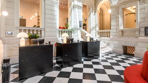 Un hall d’entrée avec un sol à carreaux, des comptoirs de réception noirs et des murs en pierre blanche.