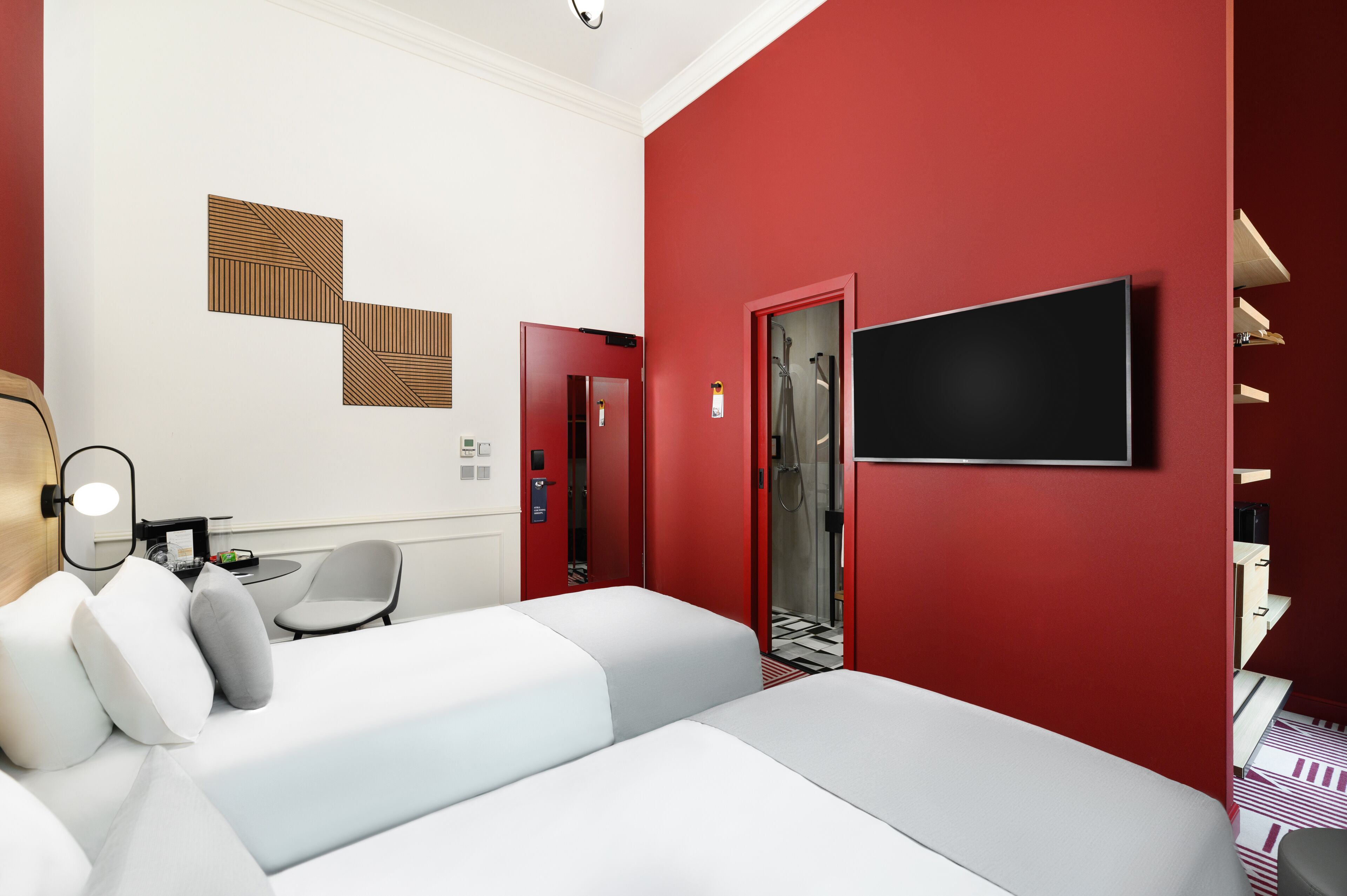 Habitación de hotel con pared de acento roja, un televisor de pantalla plana, una cama, zona de estar con cojines, una mesita y un espejo.
