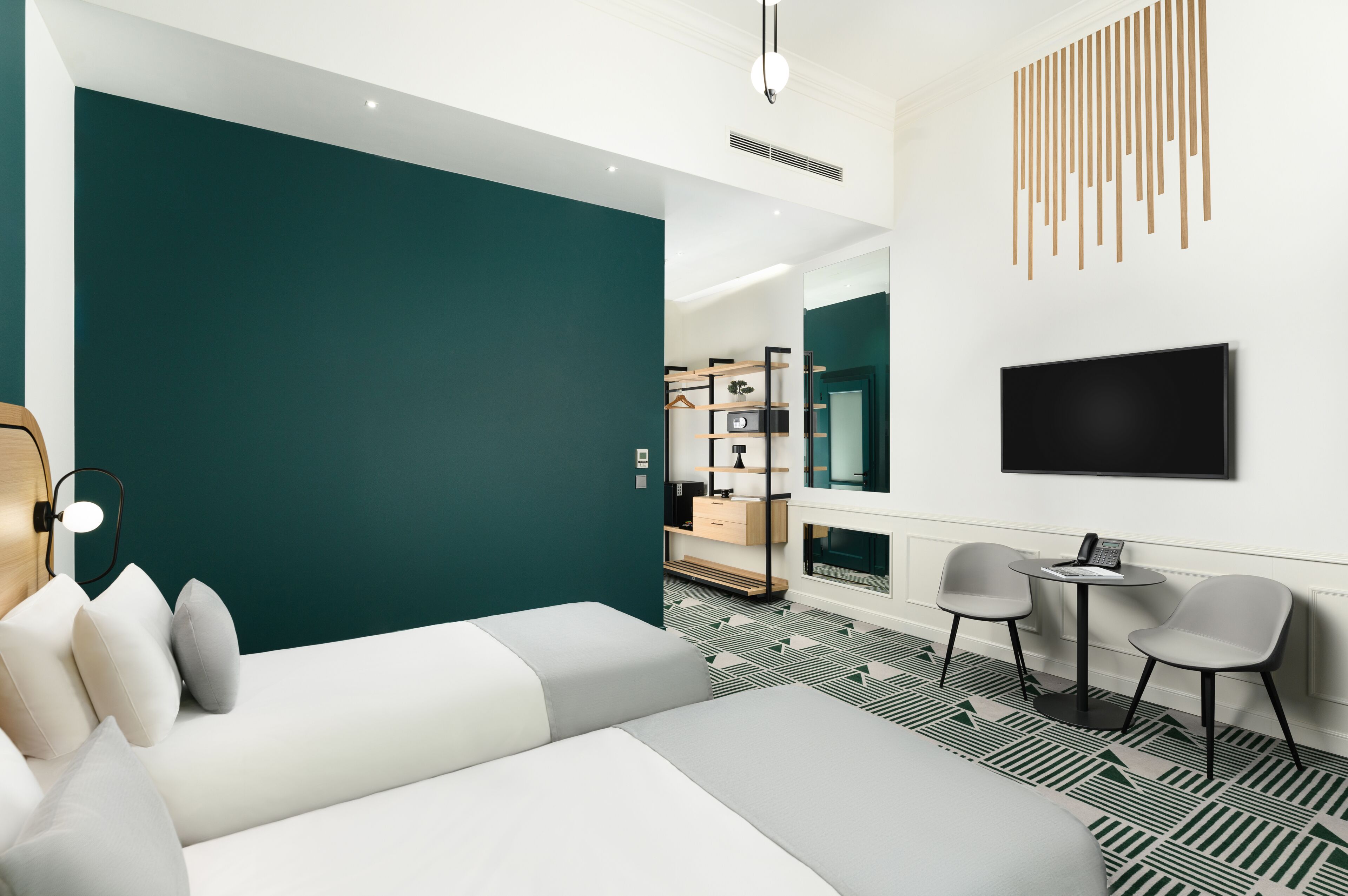 A modern hotel room with a large bed, a seating area with chairs, a TV mounted on the wall, and a small table with a phone.