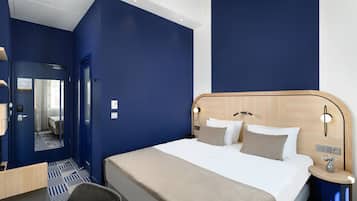 Una camera d'albergo con un letto grande, una scrivania e una sedia. Si vede uno specchio appeso alla parete e una porta che conduce a un'altra stanza.
