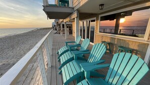 Terraza de madera con sillas Adirondack turquesas con vistas a una playa.