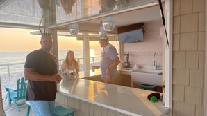 Zona de bar con vista al océano, cocina con lavaplatos y licuadora, y taburetes de bar turquesa.