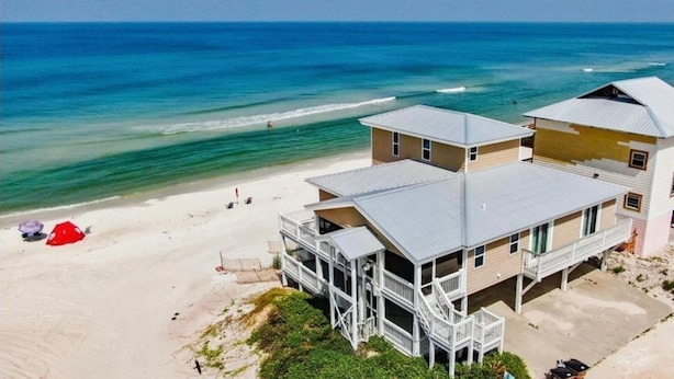 Una propiedad frente a la playa con una casa grande y un edificio más pequeño, ambos con varias terrazas y un patio cubierto.