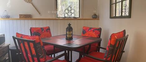 A dining area with a round table, four chairs with red cushions, a lantern, and a window with a decorative metal grille.