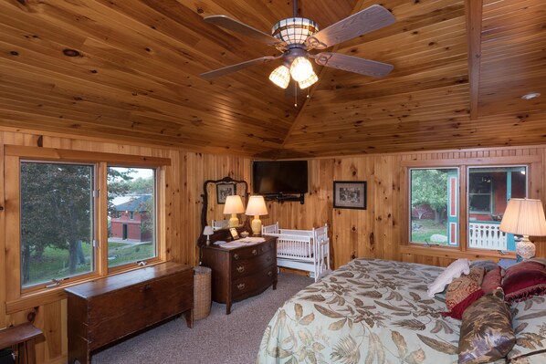 Cozy bedroom with a large bed, crib, and wooden dresser, offering a view of the outdoors and modern amenities.