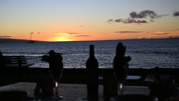A sunset view from a terrace with a table set for dining, overlooking the sea. - Pikake ocean front 20 feet from ocean (Lahaina)