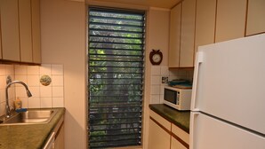 A kitchen with a window, sink, microwave, and cabinets. - Pikake ocean front 20 feet from ocean (Lahaina)