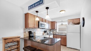 A kitchen with wooden cabinets, a granite countertop, a built-in microwave, a refrigerator, and a bar area with stools. - 🌊Great Family Condo-Pool-Steps2Beach-2BR Villas On The Gulf C5🌊 (Pensacola Beach)