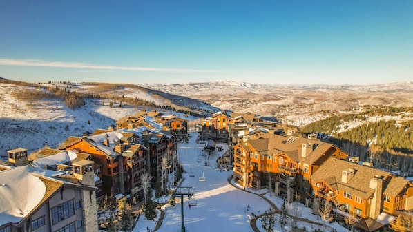A snow-covered ski resort with multiple buildings, a ski lift, and a mountainous backdrop.