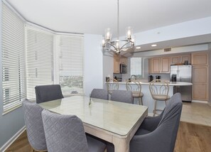A modern kitchen with a central island, a dining area with a glass table, and a chandelier. - Corner 6th Floor 3BR Condo at Silver Beach Towers! (Destin)