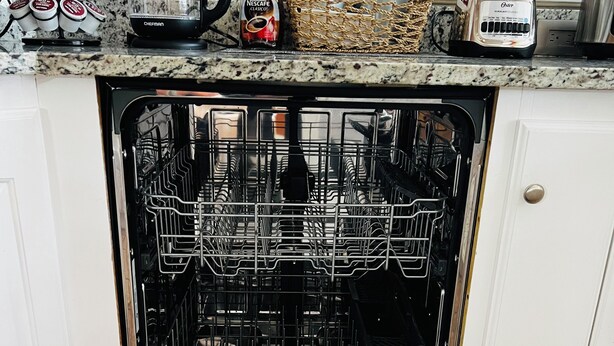 Lavavajillas abierto con diversos utensilios de cocina sobre la encimera.