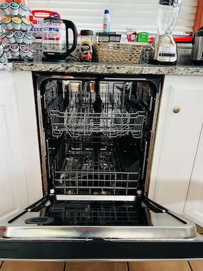 An open dishwasher with various kitchen items on the counter above.