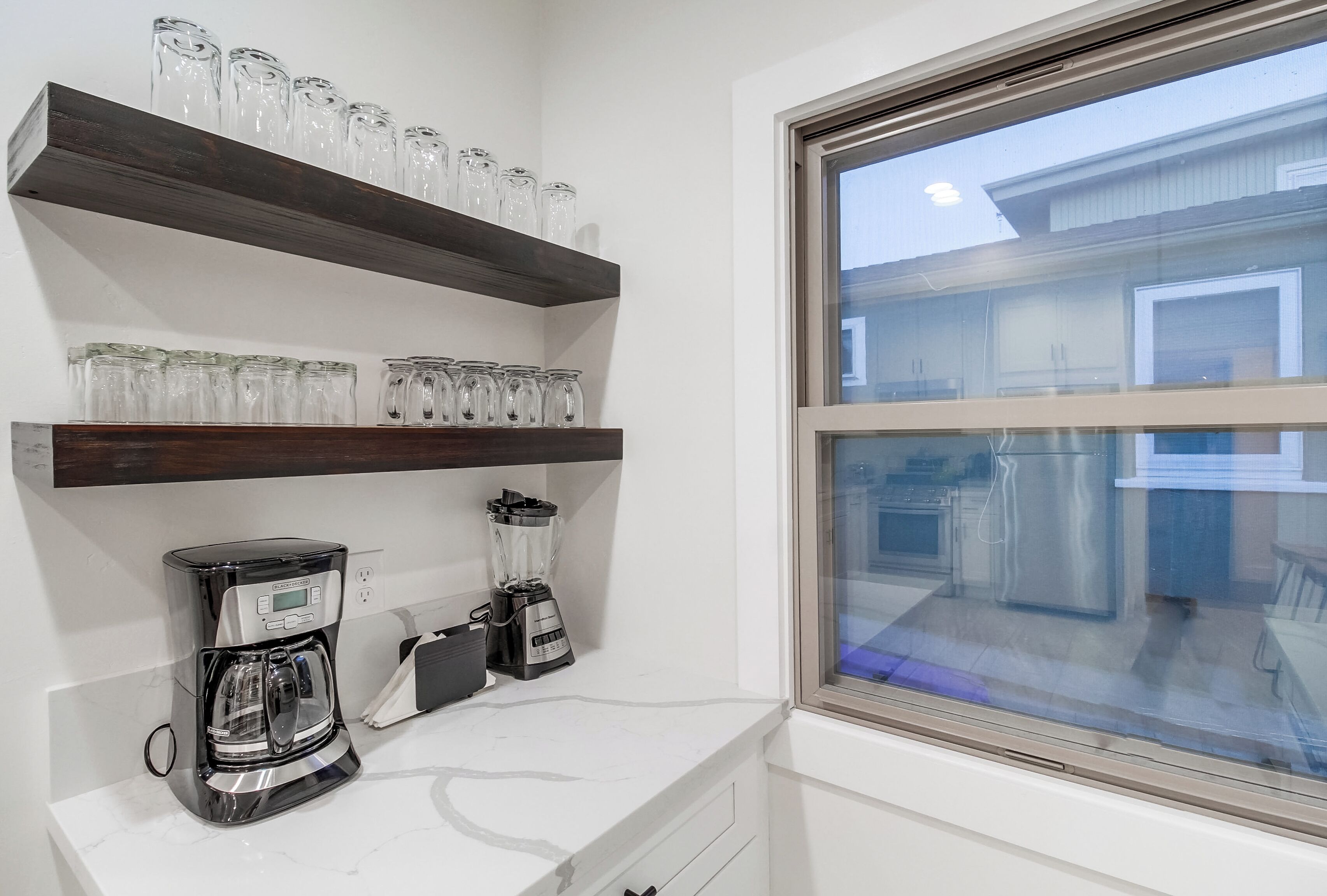 A kitchen with two coffee makers, a blender, and glass jars on shelves.